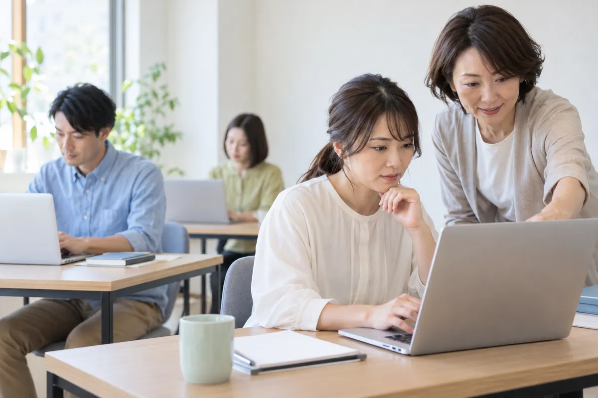 複数の受講生が学ぶ教室で講師に質問する女性